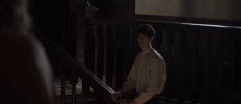 Movie still from “The Power of the Dog” (2021), directed by Jane Campion – A man sitting on top of a wooden stair railing; Medium shot, High angle