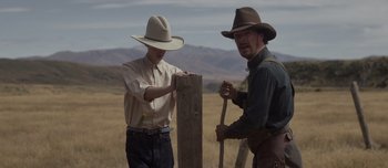 Movie still from “The Power of the Dog” (2021), directed by Jane Campion – Two men in cowboy hats are standing next to a fence post; Medium shot, Over the shoulder angle