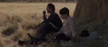 Movie still from “The Power of the Dog” (2021), directed by Jane Campion – Two people sitting in the grass near each other; Medium shot, Over the shoulder angle