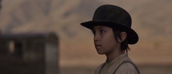 Movie still from “The Power of the Dog” (2021), directed by Jane Campion – A young boy wearing a black hat looking to his left; Close Up shot, Over the shoulder angle