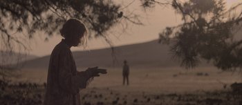 Movie still from “The Power of the Dog” (2021), directed by Jane Campion – A woman standing in a field with her hands outstreched; Medium shot, Over the shoulder angle