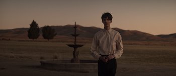 Movie still from “The Power of the Dog” (2021), directed by Jane Campion – A man standing in front of a fountain in a field; Medium shot, Over the shoulder angle