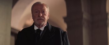 Movie still from “The Prestige” (2006), directed by Christopher Nolan – An older man wearing a suit and tie; Close Up shot, Low angle