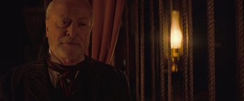 Movie still from “The Prestige” (2006), directed by Christopher Nolan – An older man standing in front of a curtain; Close Up shot, Over the shoulder angle