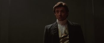 Movie still from “The Prestige” (2006), directed by Christopher Nolan – A man wearing a suit and tie standing in front of a black background; Close Up shot, Low angle