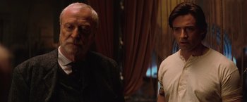 Movie still from “The Prestige” (2006), directed by Christopher Nolan – A man standing next to another man in front of a window; Medium shot, Over the shoulder angle