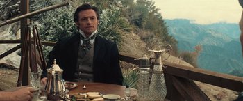 Movie still from “The Prestige” (2006), directed by Christopher Nolan – A man sitting at a table in front of mountains; Medium shot, Over the shoulder angle