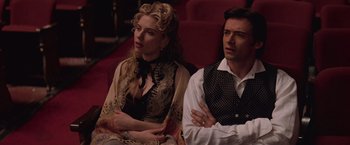 Movie still from “The Prestige” (2006), directed by Christopher Nolan – A man and a woman sitting next to each other on a couch; Medium shot, Over the shoulder angle