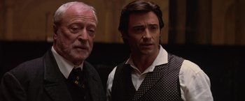 Movie still from “The Prestige” (2006), directed by Christopher Nolan – Two men standing next to each other in front of a wall; Close Up shot, Over the shoulder angle
