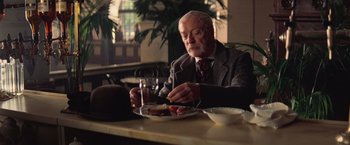 Movie still from “The Prestige” (2006), directed by Christopher Nolan – An older man sitting at a table with a plate of food in front of him; Medium shot, Over the shoulder angle