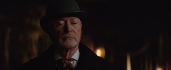 Movie still from “The Prestige” (2006), directed by Christopher Nolan – An older man wearing a hat and a tie; Close Up shot, Low angle
