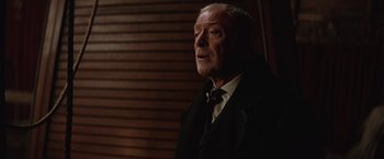 Movie still from “The Prestige” (2006), directed by Christopher Nolan – An older man wearing a suit and a tie; Close Up shot, Over the shoulder angle