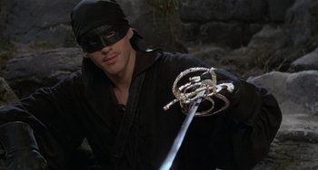 Movie still from “The Princess Bride” (1987), directed by Rob Reiner – A man wearing a black mask and holding a sword; Close Up shot, High angle