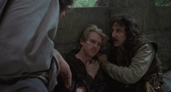 Movie still from “The Princess Bride” (1987), directed by Rob Reiner – A group of men standing around a man with long blonde hair; Medium shot, Over the shoulder angle