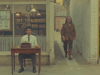 Movie still from “The Rat Catcher” (2023), directed by Wes Anderson – A man sitting at a table in front of a woman; Wide shot, Low angle