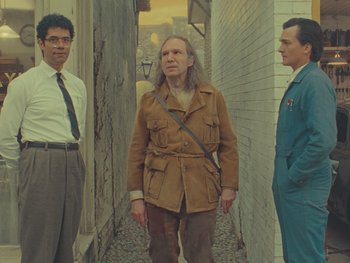 Movie still from “The Rat Catcher” (2023), directed by Wes Anderson – A group of men standing next to each other in an alleyway; Medium shot, Low angle
