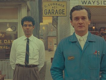 Movie still from “The Rat Catcher” (2023), directed by Wes Anderson – Two men standing next to each other in front of a building; Medium shot, Low angle