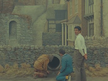 Movie still from “The Rat Catcher” (2023), directed by Wes Anderson – A painting of two men working on a sewer pipe; Wide shot, High angle