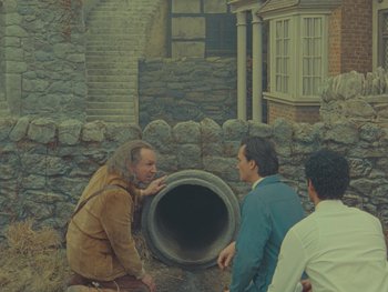 Movie still from “The Rat Catcher” (2023), directed by Wes Anderson – A group of men standing around a hole in the ground; Wide shot, High angle