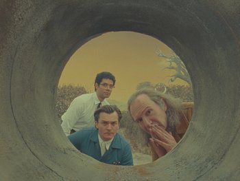 Movie still from “The Rat Catcher” (2023), directed by Wes Anderson – Three men are looking through a hole in the ground; Medium shot, Low angle