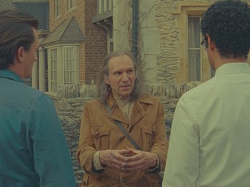 Movie still from “The Rat Catcher” (2023), directed by Wes Anderson – A man in a brown jacket standing next to two other men; Medium shot, Over the shoulder angle
