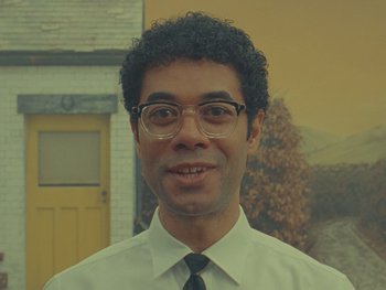 Movie still from “The Rat Catcher” (2023), directed by Wes Anderson – A man in a white dress shirt and black tie smiling; Close Up shot, Over the shoulder angle