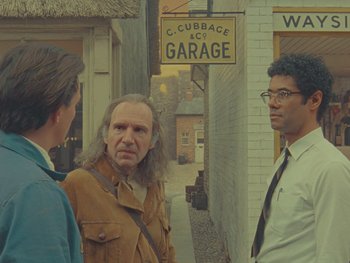 Movie still from “The Rat Catcher” (2023), directed by Wes Anderson – Three men standing on the sidewalk in front of a garage; Medium shot, Over the shoulder angle
