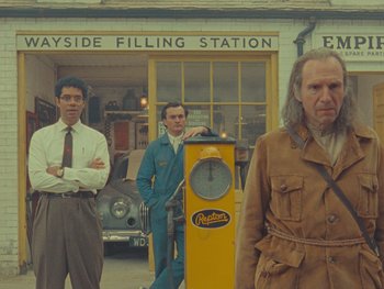Movie still from “The Rat Catcher” (2023), directed by Wes Anderson – A group of men standing in front of a gas station; Medium shot, Low angle