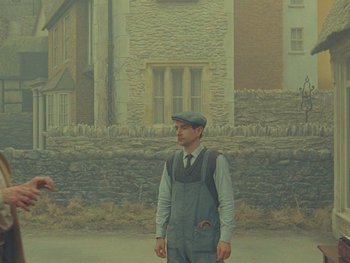 Movie still from “The Rat Catcher” (2023), directed by Wes Anderson – A man standing in front of a stone building; Wide shot, Over the shoulder angle