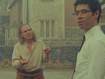 Movie still from “The Rat Catcher” (2023), directed by Wes Anderson – Two men standing next to each other in front of a stone building; Medium shot, Over the shoulder angle