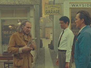 Movie still from “The Rat Catcher” (2023), directed by Wes Anderson – A man in a brown jacket talking to two other men; Medium shot, Over the shoulder angle