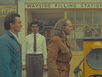 Movie still from “The Rat Catcher” (2023), directed by Wes Anderson – A group of men standing in front of a building; Medium shot, Over the shoulder angle