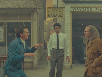 Movie still from “The Rat Catcher” (2023), directed by Wes Anderson – A group of men standing on the side of a road; Wide shot, Over the shoulder angle