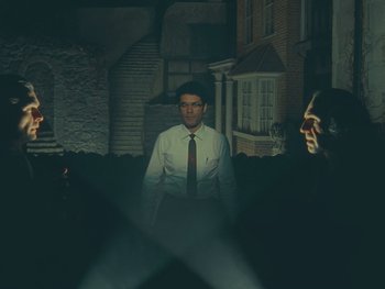 Movie still from “The Rat Catcher” (2023), directed by Wes Anderson – A man in a suit and tie standing next to a woman; Wide shot, Low angle