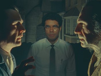 Movie still from “The Rat Catcher” (2023), directed by Wes Anderson – A man standing in front of two other men in a room; Medium shot, Over the shoulder angle