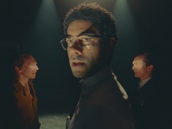 Movie still from “The Rat Catcher” (2023), directed by Wes Anderson – A man with glasses is standing between two other men; Medium shot, Low angle