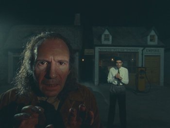 Movie still from “The Rat Catcher” (2023), directed by Wes Anderson – A man standing next to another man in front of a building at night; Medium shot, Over the shoulder angle