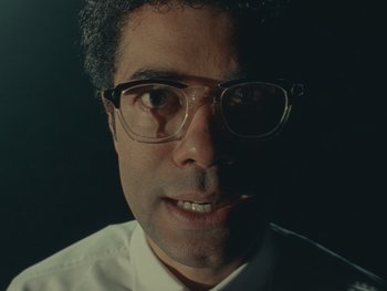 Movie still from “The Rat Catcher” (2023), directed by Wes Anderson – A person wearing glasses and a white shirt; Close Up shot, Low angle