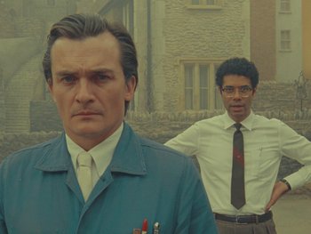 Two men standing next to each other in front of a brick building