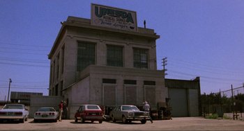 Movie still from “The Return of the Living Dead” (1985), directed by Dan O'Bannon – An old photo of an old building with cars parked in front of it; Extreme Wide shot, Low angle