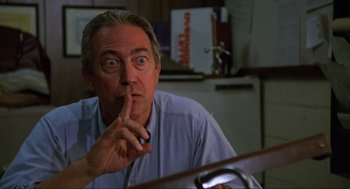 Movie still from “The Return of the Living Dead” (1985), directed by Dan O'Bannon – A person sitting at a table holding his index finger to his lips; Close Up shot, Over the shoulder angle