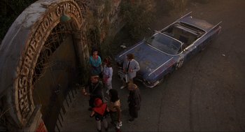Movie still from “The Return of the Living Dead” (1985), directed by Dan O'Bannon – A group of people standing next to an old blue car; Wide shot, High angle