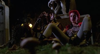Movie still from “The Return of the Living Dead” (1985), directed by Dan O'Bannon – Two women sitting on the ground with a cigarette in their mouth; Medium shot, Low angle