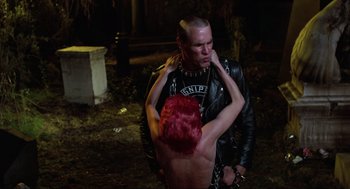 Movie still from “The Return of the Living Dead” (1985), directed by Dan O'Bannon – A man in a leather jacket holding a woman in a red wig; Medium shot, Over the shoulder angle