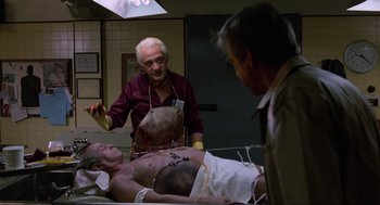 Movie still from “The Return of the Living Dead” (1985), directed by Dan O'Bannon – A man is lying on a bed while two other men look on; Medium shot, Over the shoulder angle