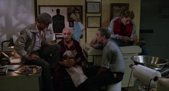 Movie still from “The Return of the Living Dead” (1985), directed by Dan O'Bannon – A group of men sitting around in a room; Wide shot, High angle