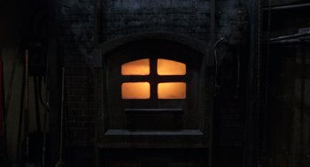 Movie still from “The Return of the Living Dead” (1985), directed by Dan O'Bannon – A window in a building with a light shining on it; Wide shot, Low angle