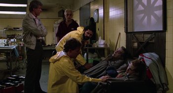 Movie still from “The Return of the Living Dead” (1985), directed by Dan O'Bannon – A group of people standing around a man laying in a bed; Medium shot, High angle