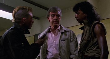 Movie still from “The Return of the Living Dead” (1985), directed by Dan O'Bannon – A man in a trench coat talking to two other men; Medium shot, Over the shoulder angle