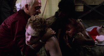 Movie still from “The Return of the Living Dead” (1985), directed by Dan O'Bannon – A group of people in a room with a man in the middle of the room; Close Up shot, Over the shoulder angle